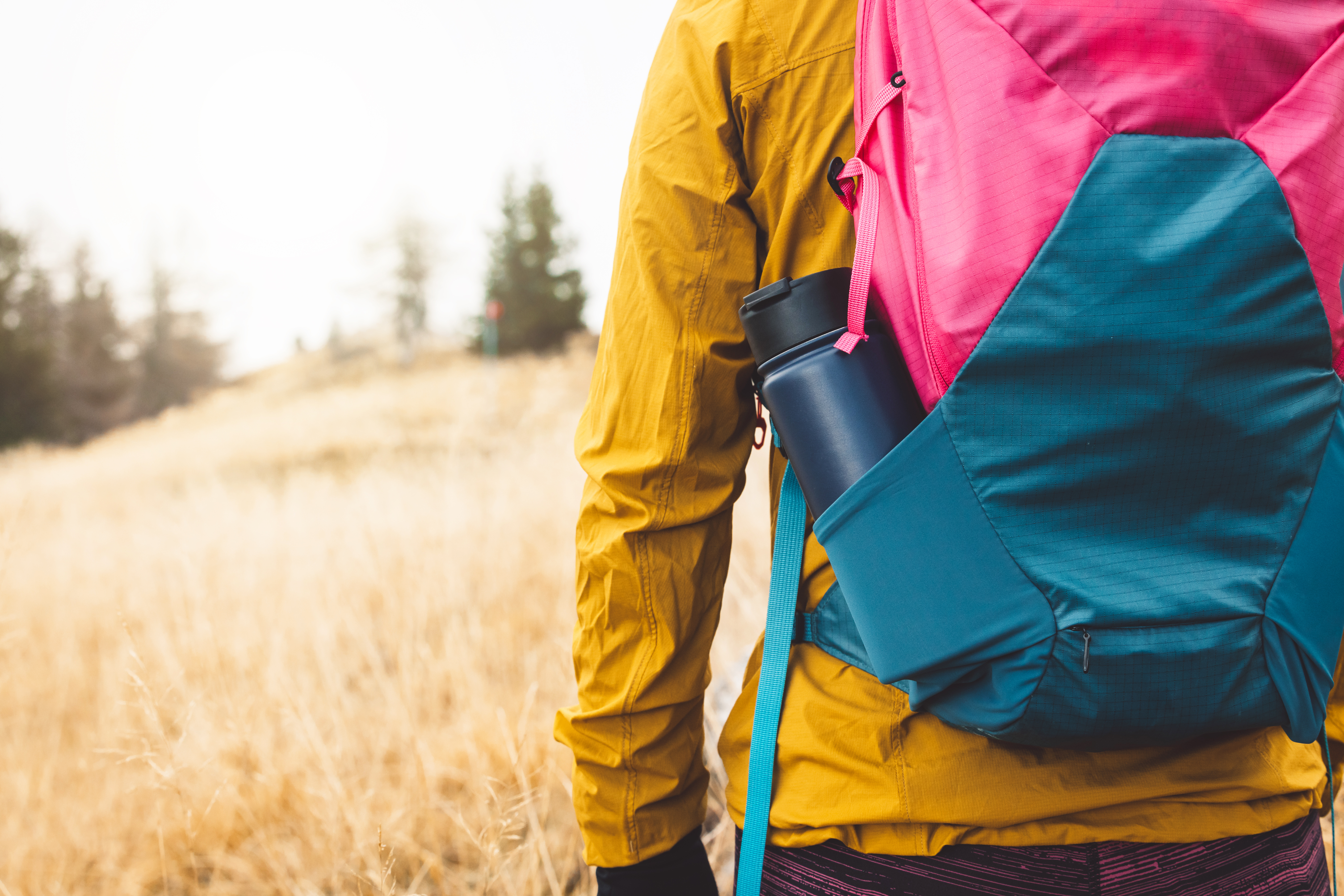 Close up view from the back unrecognizable woman with a pink and blue backpack with thermo flask sticking out of the side pocket